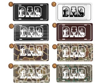 May include: License plates with the word "DAD" and a deer silhouette. The plates come in various designs, including black, white, brown, camouflage, and an American flag pattern. The plates are rectangular with rounded corners.