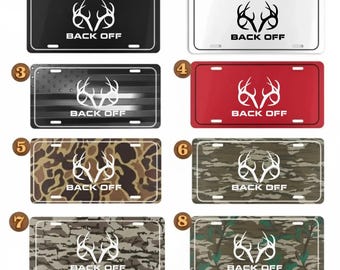 May include: A collection of license plates in various colors and patterns. Each plate features a white antler design and the text "BACK OFF". The plates include black, white, red, camouflage, and a design with an American flag.