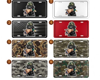 May include: License plates featuring a black Labrador Retriever wearing a camouflage hat and holding a duck. The plates come in various colors and patterns, including black, white, red, and camouflage designs. A great gift for dog lovers and hunters.