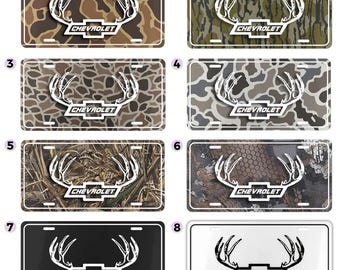 May include: A collection of eight license plates featuring a white deer antler design and the Chevrolet logo. The plates have various camouflage patterns, including brown, green, and gray, and solid black and white options.