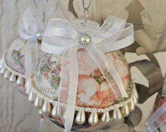 Pale peach floral patterned Christmas ornament surrounded by and terminated in "pearls". Focal "gem" at center of clear and white bow.