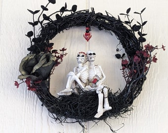 Black 10" wreath with lovely skeleton couple adorned with roses and a heart strung above their heads. Great Halloween decor.