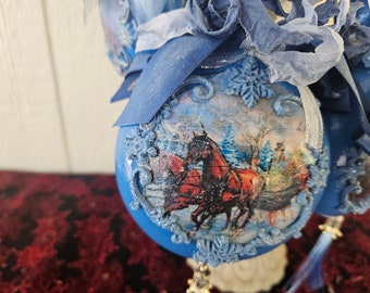 Blue disc ornaments with 8 different winter scenes, all including horses and framed in ornate swirls topped with 3 shades of antiqued ribbon