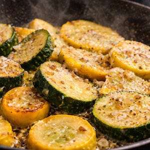May include: Close-up of a pan filled with sliced zucchini and yellow squash, seasoned and cooked. The vegetables are golden brown and green, with visible seasoning and steam rising from the pan. A culinary image.