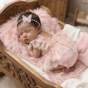 Puede incluir: Un beb&eacute; dormido con un vestido rosa con detalles de mariposas y una diadema a juego. El beb&eacute; est&aacute; acostado sobre una manta rosa esponjosa dentro de una cuna de madera con detalles tallados. El vestido tiene estrellas doradas.