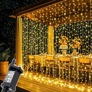 May include: Warm white string lights create a curtain effect in an outdoor dining area. The lights hang vertically. A black power adapter is in the foreground. The scene includes a table setting with flowers and chairs, creating a cozy atmosphere.