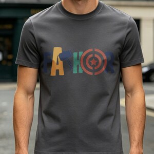 May include: Dark gray t-shirt with the word "THOR" in colorful block letters. The "T" is orange, the "H" has a hammer design, the "O" is a target, and the "R" is blue. The shirt is short-sleeved.