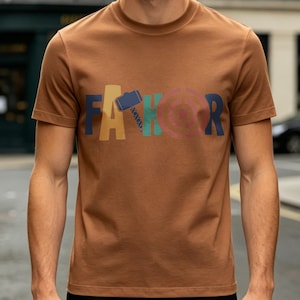 May include: A brown t-shirt with the word "FAКОR" in colorful block letters. The "A" is yellow, the "K" is teal, and the "R" is navy blue. The "O" is pink with a target design.