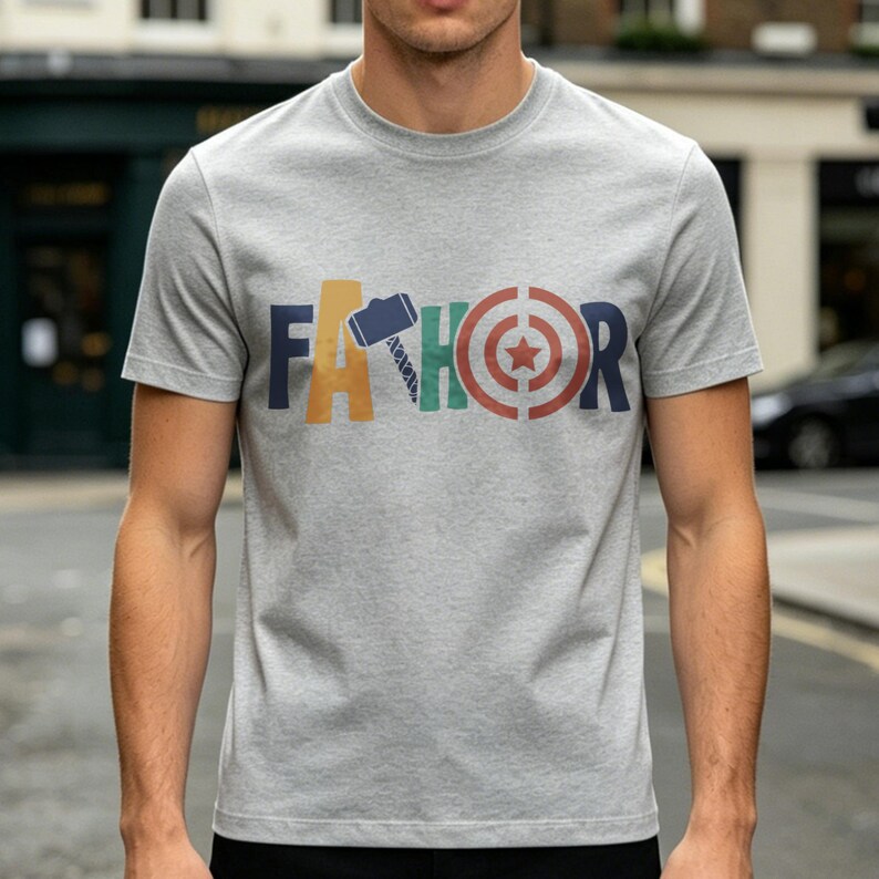 May include: A gray t-shirt with the word "FA THOR" printed across the chest in colorful block letters. The letters are designed with superhero-themed graphics, including a hammer, a target, and a saw.