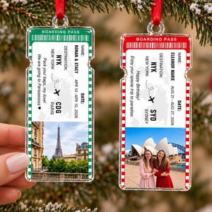 May include: Two rectangular acrylic ornaments shaped like boarding passes with red ribbons. The green one features text for Ronan & Stacy, a Paris trip, and the Eiffel Tower. The red one features text for Eleanor Marie, a Sydney trip, and a photo of two people.