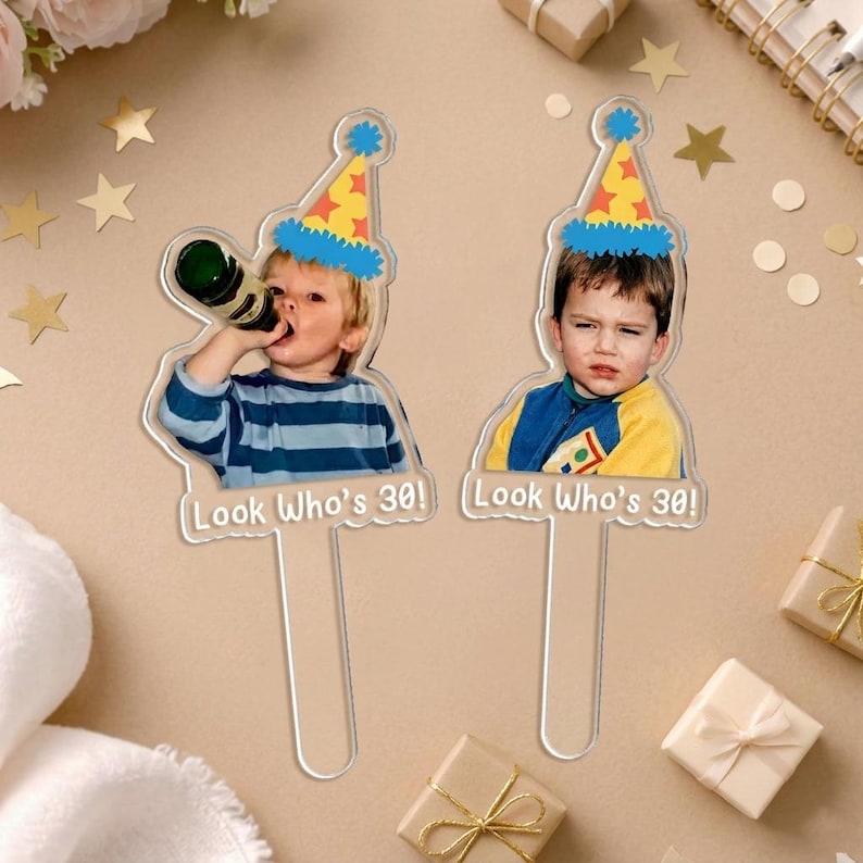May include: Two clear acrylic cake toppers with images of a young person wearing a party hat. One is drinking from a bottle. The text "Look Who's 30!" is at the bottom of each topper.