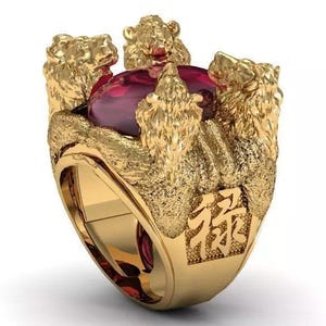 May include: A gold ring featuring a large, oval-cut deep red gemstone set in the center. The band is adorned with four sculpted lion heads facing outward, and the side of the band displays a square panel with the Chinese character 禄 engraved.