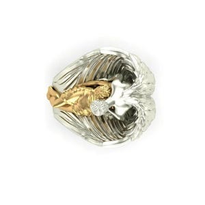 May include: A detailed ring featuring a gold-colored figure cradled within silver-colored wings. The ring's design showcases intricate feather detailing and a contrasting color scheme, creating a striking visual effect. The ring is a piece of jewelry.