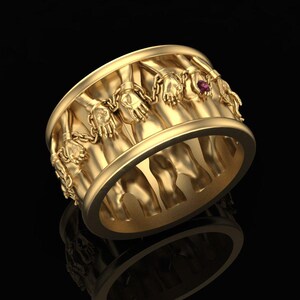 Könnte beinhalten: Ein goldfarbener Ring mit einem detaillierten Design, das Hände und Ketten zeigt. Ein kleiner, runder, violetter Edelstein ist in die Oberfläche des Rings eingesetzt. Der Ring hat eine polierte Oberfläche und wird vor schwarzem Hintergrund präsentiert.