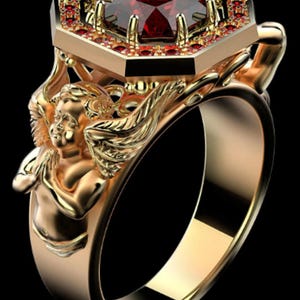 Peut inclure: Une bague en or ornée d'une grande pierre précieuse hexagonale rouge foncé au centre, entourée d'une bordure de petites pierres rouges. L'anneau présente une figurine de chérubin ailé sculptée, les mains jointes en prière sur le côté.