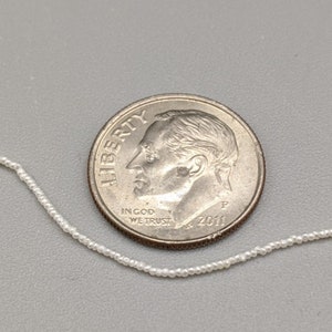 May include: A white pearl necklace with a US dime coin for scale. The coin is dated 2011 and has the words "Liberty" and "In God We Trust" on it.