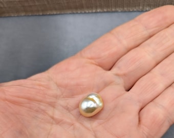 May include: A large, off-white, pearlescent, irregularly shaped pearl. The pearl has a slight golden hue.