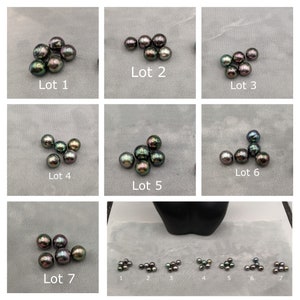 May include: Seven lots of black and green Tahitian pearls, each lot containing a different number of pearls. The pearls are arranged in a cluster on a grey surface. The lots are numbered 1 through 7.