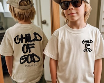 May include: Two children wearing cream-colored t-shirts with the text "CHILD OF GOD" in black. One shirt has the text on the back and the front, the other has the text on the front. The text "PSALM 23" is below the text on the back of one shirt.