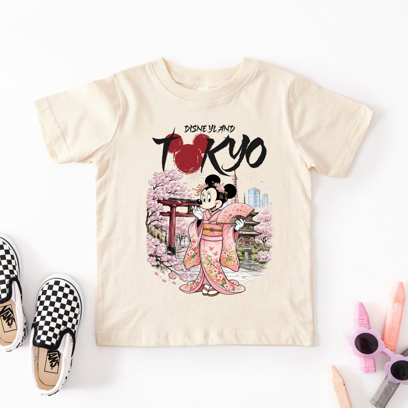 May include: Cream-colored t-shirt featuring a graphic of Minnie Mouse in a pink kimono, holding a fan, with a Japanese temple and cherry blossoms. The text "Disneyland Tokyo" is above the image.