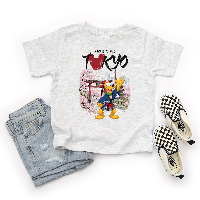 May include: A light gray t-shirt featuring a graphic of Pluto in a Japanese kimono with the text "Disneyland Tokyo". The shirt is paired with light wash denim jeans and black and white checkered slip-on sneakers.
