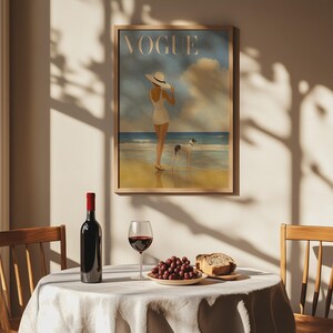 May include: A framed "Vogue" magazine cover art print featuring a woman in a white swimsuit and hat on a beach with a dog. A bottle of red wine, a glass of wine, grapes, and bread are on a table.