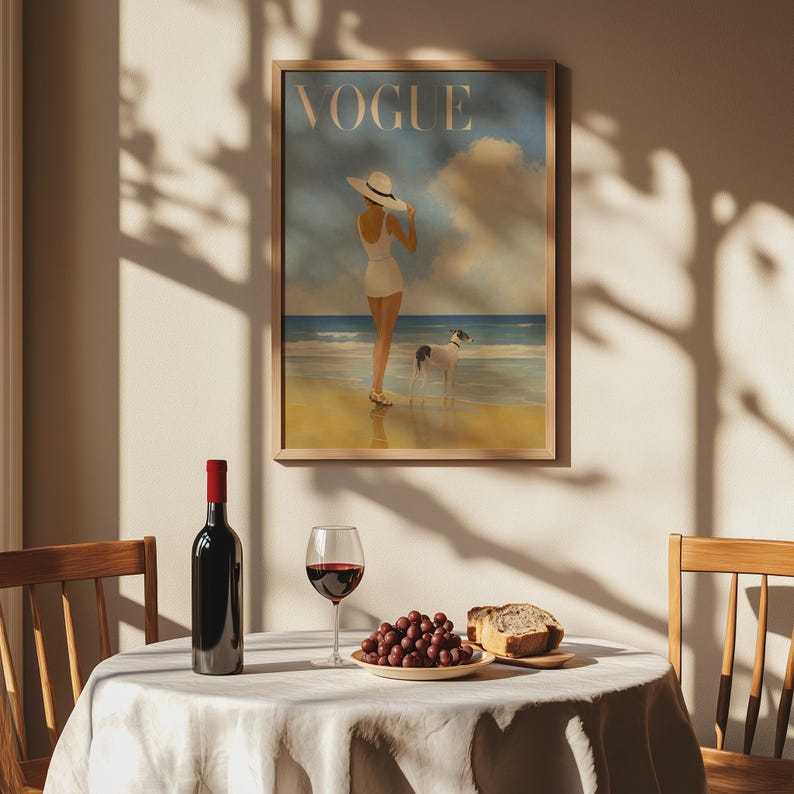 May include: A framed "Vogue" magazine cover art print featuring a woman in a white swimsuit and hat on a beach with a dog. A bottle of red wine, a glass of wine, grapes, and bread are on a table.