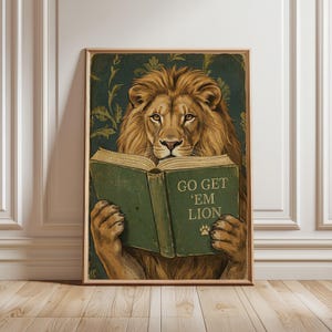 May include: A framed print featuring a lion reading a book with the text "GO GET 'EM LION". The lion has a golden mane and is set against a dark green background with a floral pattern. The book is green with white text.
