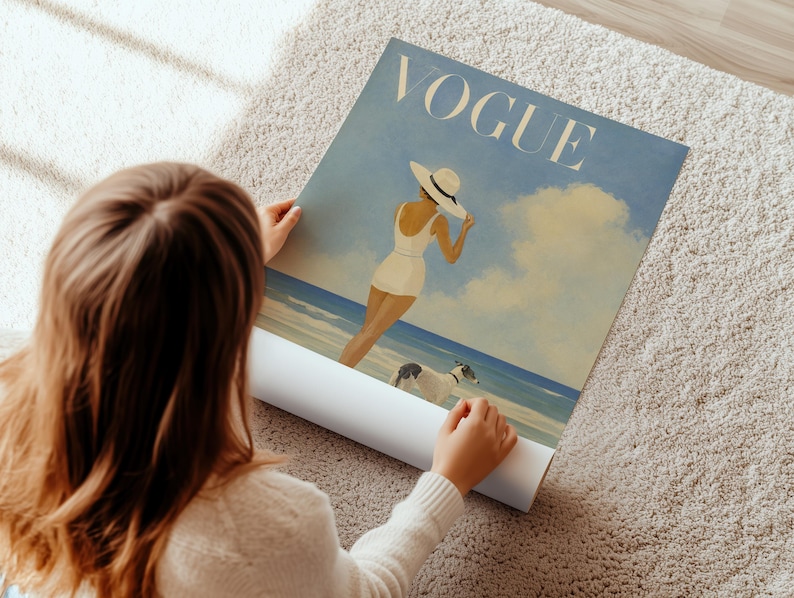 May include: A rolled-up Vogue poster featuring a vintage illustration of a woman in a white swimsuit and hat on a beach with two dogs. The poster has a blue and beige color scheme.