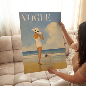 May include: A canvas print of a vintage Vogue magazine cover. The artwork depicts a woman in a white swimsuit and hat on a beach with a dog. The word "VOGUE" is printed in large, light-colored letters at the top.