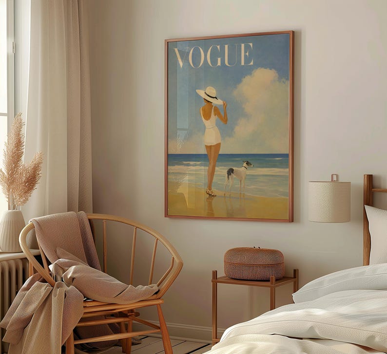 May include: A framed Vogue magazine cover art print. The artwork depicts a person in a white swimsuit and hat standing on a beach with a dog. The word "VOGUE" is at the top in white letters. The background features a blue sky and ocean.