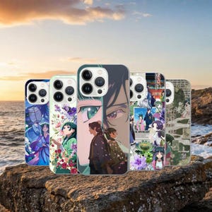 May include: A collection of five phone cases featuring anime-style illustrations. The cases display various colorful designs, including characters, floral patterns, and scenes. The cases are shown on a rock formation with a sunset backdrop.
