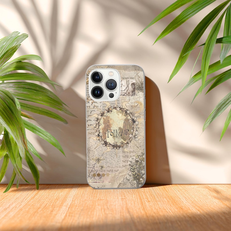 May include: A beige phone case with a vintage map design. The case features a circular floral wreath with the word "FOLKIR" in the center. The case has a matte finish and is set against a wooden surface with green foliage.