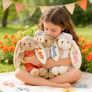 May include: A young person embraces three plush bunny rabbits. Each bunny has long ears and is personalized with a name embroidered on one ear: "Lea", "Ava", and "Ben". The bunnies are in shades of brown, beige, and white, with colorful outfits.