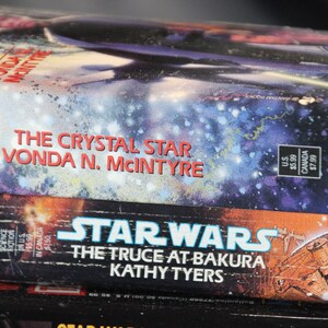 May include: Stack of Star Wars science fiction novels. The top book is "The Crystal Star" by Vonda N. McIntyre, with a space scene cover. Below is "The Truce at Bakura" by Kathy Tyers. The books are in good condition.