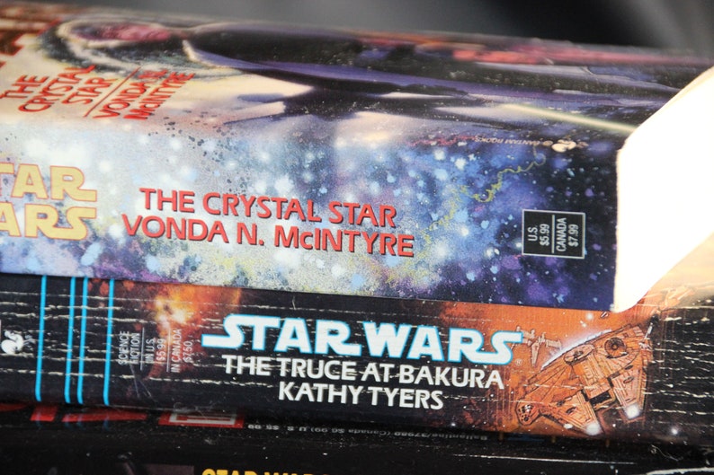 May include: Stack of Star Wars science fiction novels. The top book is "The Crystal Star" by Vonda N. McIntyre, with a space scene cover. Below is "The Truce at Bakura" by Kathy Tyers. The books are in good condition.