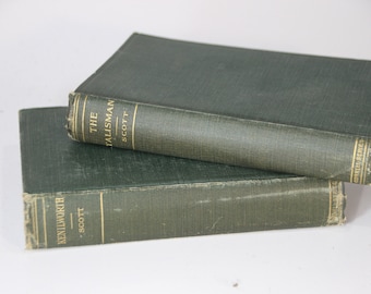 May include: Two antique books with dark green covers are stacked on a white surface. The top book is titled "The Talisman" by Scott, with gold lettering. The bottom book is titled "Kenilworth" by Scott. The books have aged, worn edges.