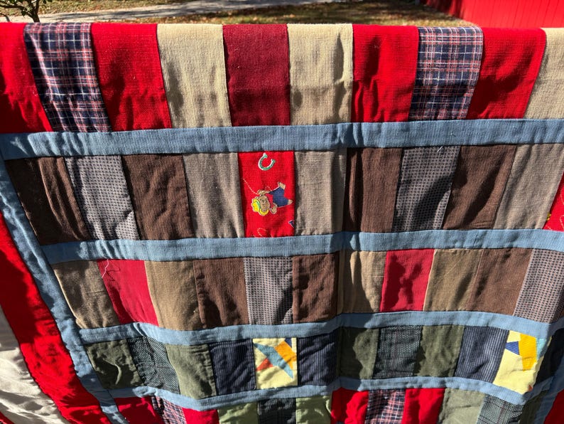 May include: A patchwork quilt with a variety of fabrics in red, blue, brown, and beige. The quilt features a red border and blue denim-like strips. Some patches have embroidered details, including a horseshoe.