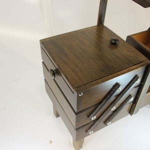 Puede incluir: Una caja de costura de madera vintage con un acabado marr&oacute;n oscuro. La caja tiene una tapa con bisagras, m&uacute;ltiples cajones y un asa para transportar. Los cajones est&aacute;n dise&ntilde;ados para expandirse hacia afuera. La caja est&aacute; elevada sobre peque&ntilde;as patas de madera.