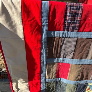 May include: A handmade quilt with a patchwork design. The quilt features a variety of fabrics in red, beige, blue, brown, and plaid patterns. The quilt is made of corduroy and other fabrics.