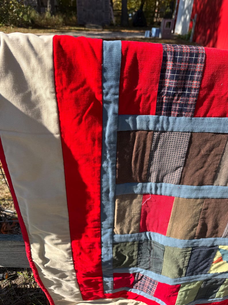 May include: A handmade quilt with a patchwork design. The quilt features a variety of fabrics in red, beige, blue, brown, and plaid patterns. The quilt is made of corduroy and other fabrics.
