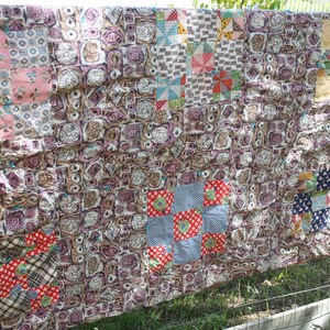 May include: A handmade quilt with a patchwork design, featuring squares of various patterns and colors. The quilt is primarily brown with accents of pink, red, blue, and yellow. It is hanging outdoors, showcasing its intricate details and craftsmanship.