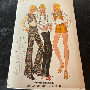 Pode incluir: Padrão de costura vintage com ilustrações de três mulheres em trajes dos anos 70. O padrão inclui designs para tops, coletes, calças e shorts. A capa exibe o texto "Dawnick" e "Junior Petite & Misses'" com informações de tamanho e preço.