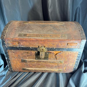 May include: A vintage wooden chest with a leather exterior. The chest has a brass lock and metal accents. The leather is worn and has a distressed look.