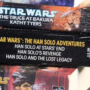 May include: Close-up of three Star Wars books. The top book is "The Truce at Bakura" by Kathy Tyers. The middle book is "Star Wars: The Han Solo Adventures" with titles "Han Solo at Stars' End", "Han Solo's Revenge", and "Han Solo and the Lost Legacy".