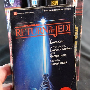 May include: A copy of the book "Star Wars: Return of the Jedi" by James Kahn. The cover features a blue and white lightsaber against a blue background. The book is a special book club edition.
