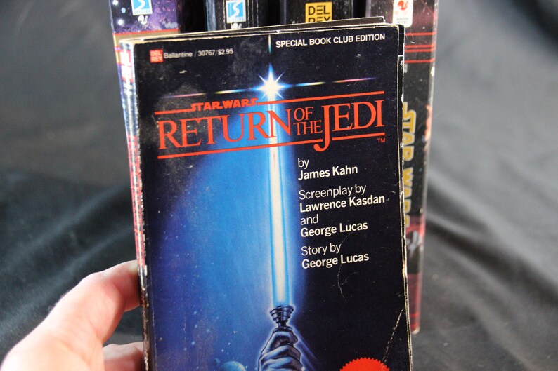 May include: A copy of the book "Star Wars: Return of the Jedi" by James Kahn. The cover features a blue and white lightsaber against a blue background. The book is a special book club edition.