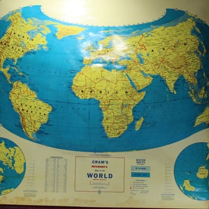 May include: A vintage world map, featuring a blue ocean and yellow continents. The map includes North and South Polar projections and text that reads "Cram's Beginner's Map of the World."