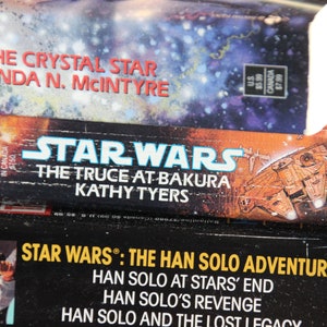 May include: Stacked Star Wars books featuring titles like "The Crystal Star" and "The Truce at Bakura." The covers display space-themed artwork and the Star Wars logo. The books are science fiction novels.