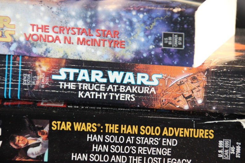 May include: Stacked Star Wars books featuring titles like "The Crystal Star" and "The Truce at Bakura." The covers display space-themed artwork and the Star Wars logo. The books are science fiction novels.
